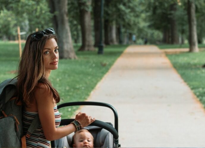 Młoda kobieta z dzieckiem w wózku spaceruje po parku