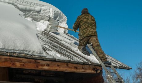 Mężczyzna odśnieża drewniany dach - usuwa grubą warstwę śniegu