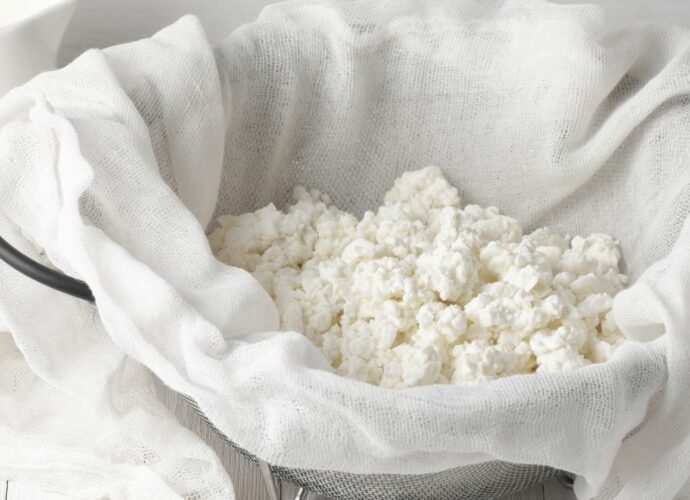Domowy twaróg z mleka odcieka na durszlaku wyłożonym gazą
