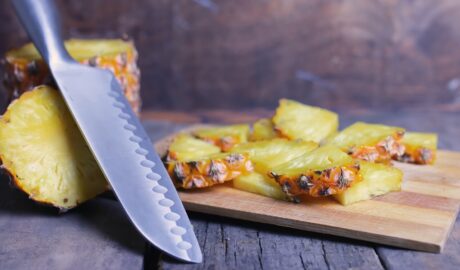 Ananas pokrojony w plasterki ułożony na drewnianej desce, obok noża