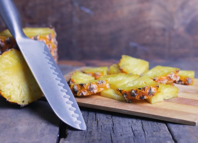 Ananas pokrojony w plasterki ułożony na drewnianej desce, obok noża
