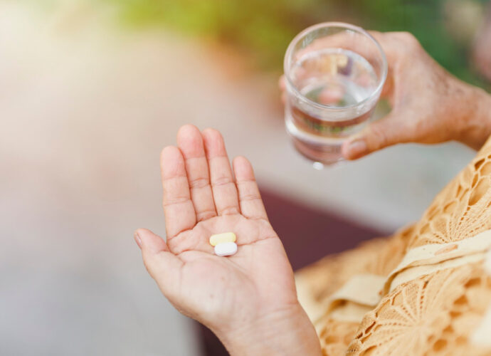 Kobieta trzyma na dłoni kilka suplementów w tabletkach oraz szklankę wody