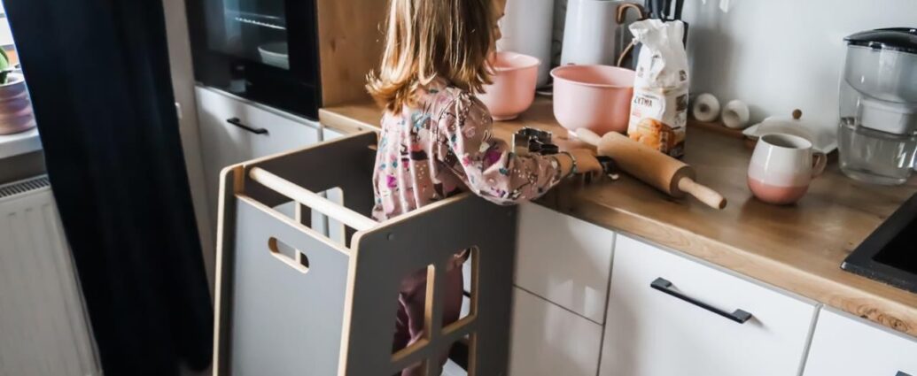 Małą dziewczynka przy kuchennym blacie bezpiecznie bawi się w kuchni w pomocniku kuchennym