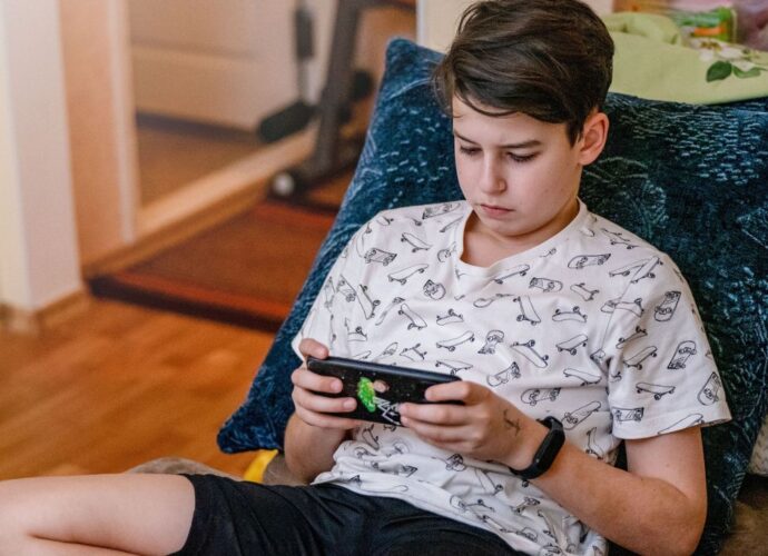 Nastolatek ze smartfonem na łóżku z pościelą