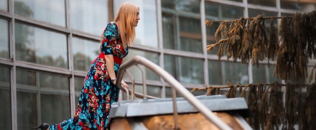 Kobieta w sukience w kwiaty stoi na schodach przed budynkiem