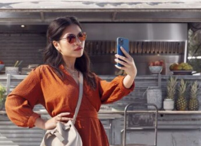 Kobieta w okularach przeciwsłonecznych przegląda wiadomości na smartfonie