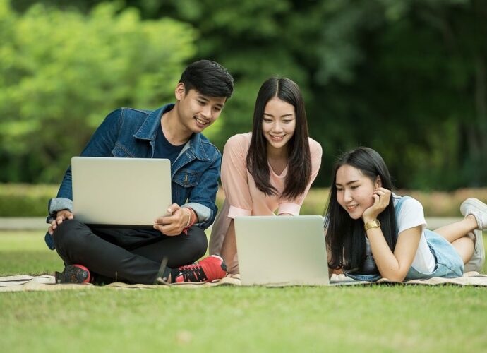 Studenci z laptopami na trawniku w parku