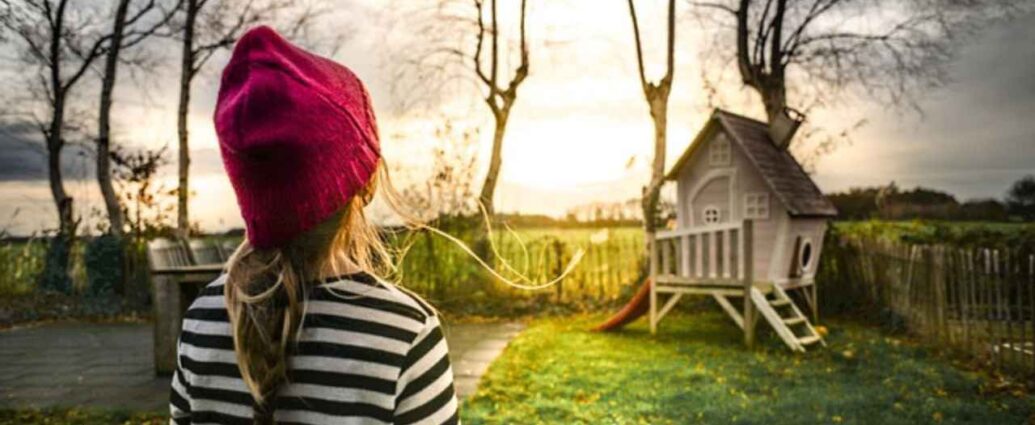 Dziewczynka w ogrodzie z drewnianym domkiem ogrodowym