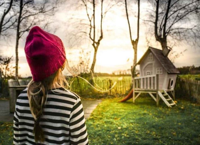 Dziewczynka w ogrodzie z drewnianym domkiem ogrodowym