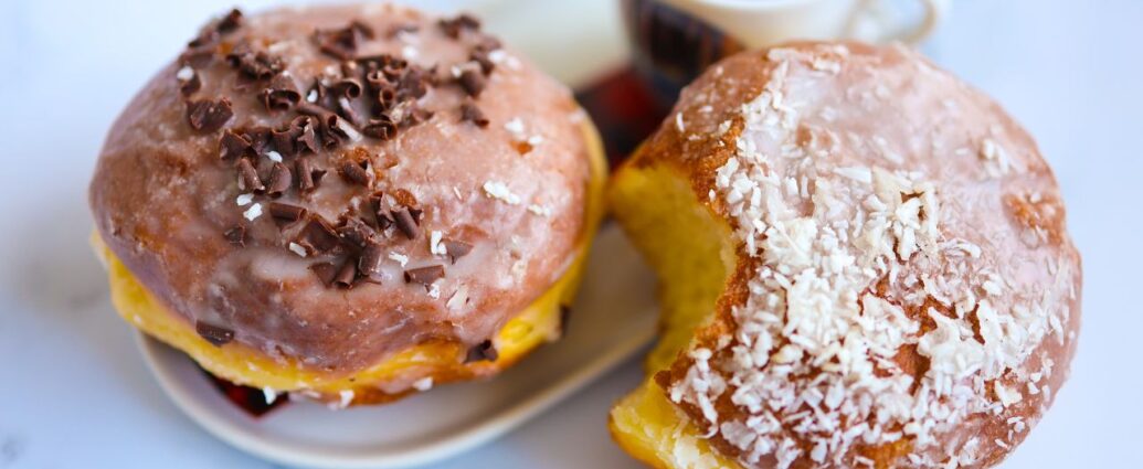 Pączek z cukrem pudrem i pączek z lukrem na talerzyku, podane z filiżanką kawy