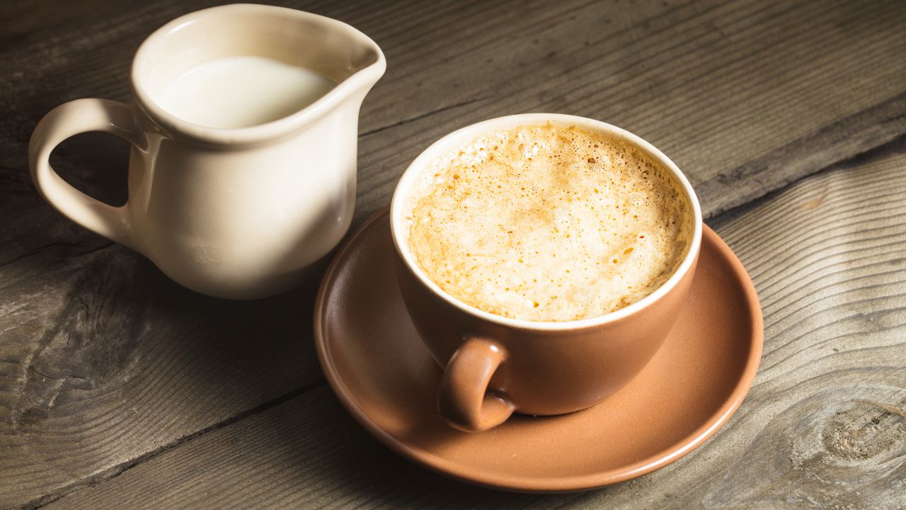 Filiżanka kawy z mlekiem, obok mlecznik