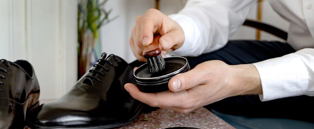 Dłonie nabierające pastę szczotką do pastowania czarnych butów wizytowych derby