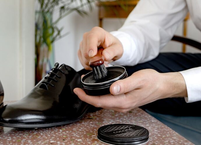 Dłonie nabierające pastę szczotką do pastowania czarnych butów wizytowych derby