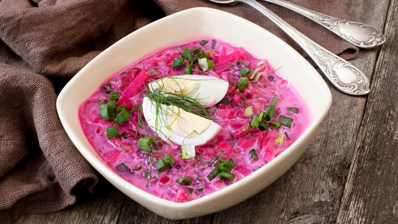 Chłodnik z buraczków w białej misce, podany z jajkiem na twardo, koperkiem i cebulką dymką