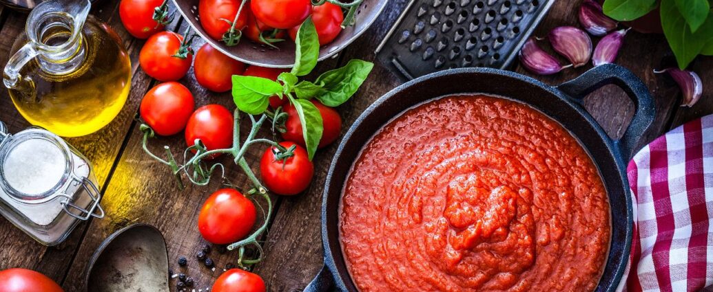 Pomidory w różnej postaci - świeże owoce na gałązce oraz przecier pomidorowy w garnku. Które zawierają więcej likopenu?