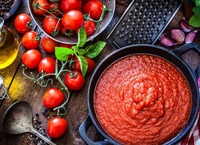 Pomidory w różnej postaci - świeże owoce na gałązce oraz przecier pomidorowy w garnku. Które zawierają więcej likopenu?