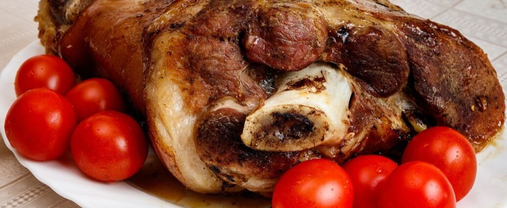 Pieczona golonka podana na półmisku, udekorowana pomidorkami koktajlowymi