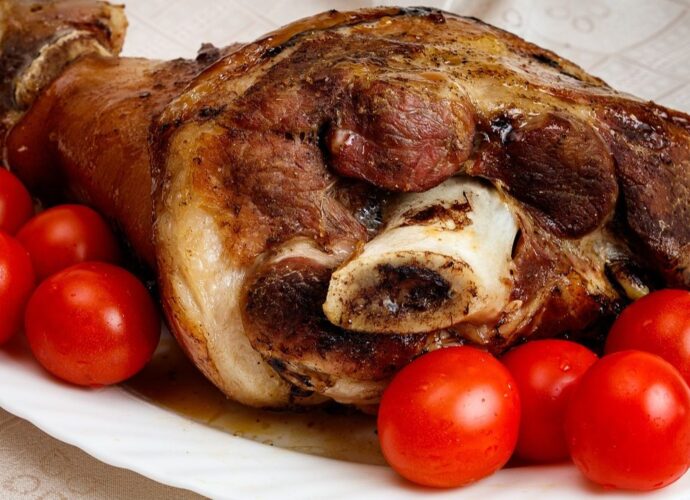 Pieczona golonka podana na półmisku, udekorowana pomidorkami koktajlowymi