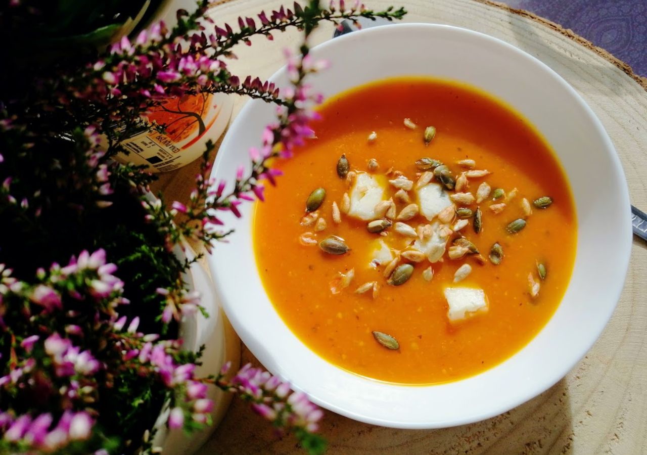 Zupa dyniowa podana w białej misce, podana z pestkami słonecznika, pestkami dyni i serem feta