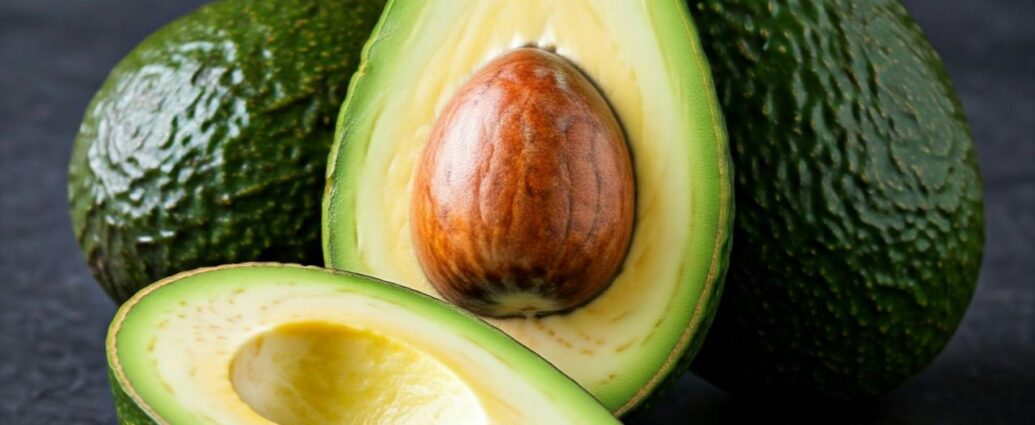 Owoce zielonego awokado ze skórką oraz przecięte na połówki z widoczną pestką i miąższem
