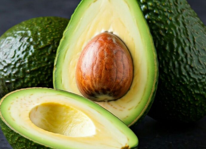 Owoce zielonego awokado ze skórką oraz przecięte na połówki z widoczną pestką i miąższem